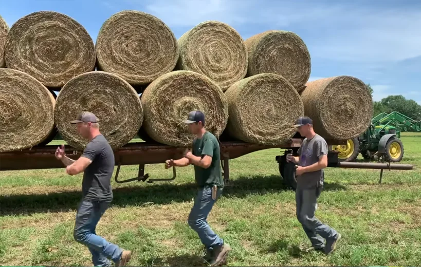 The Peterson Farm Bros standing infront of a trucl loaded with round hay bales